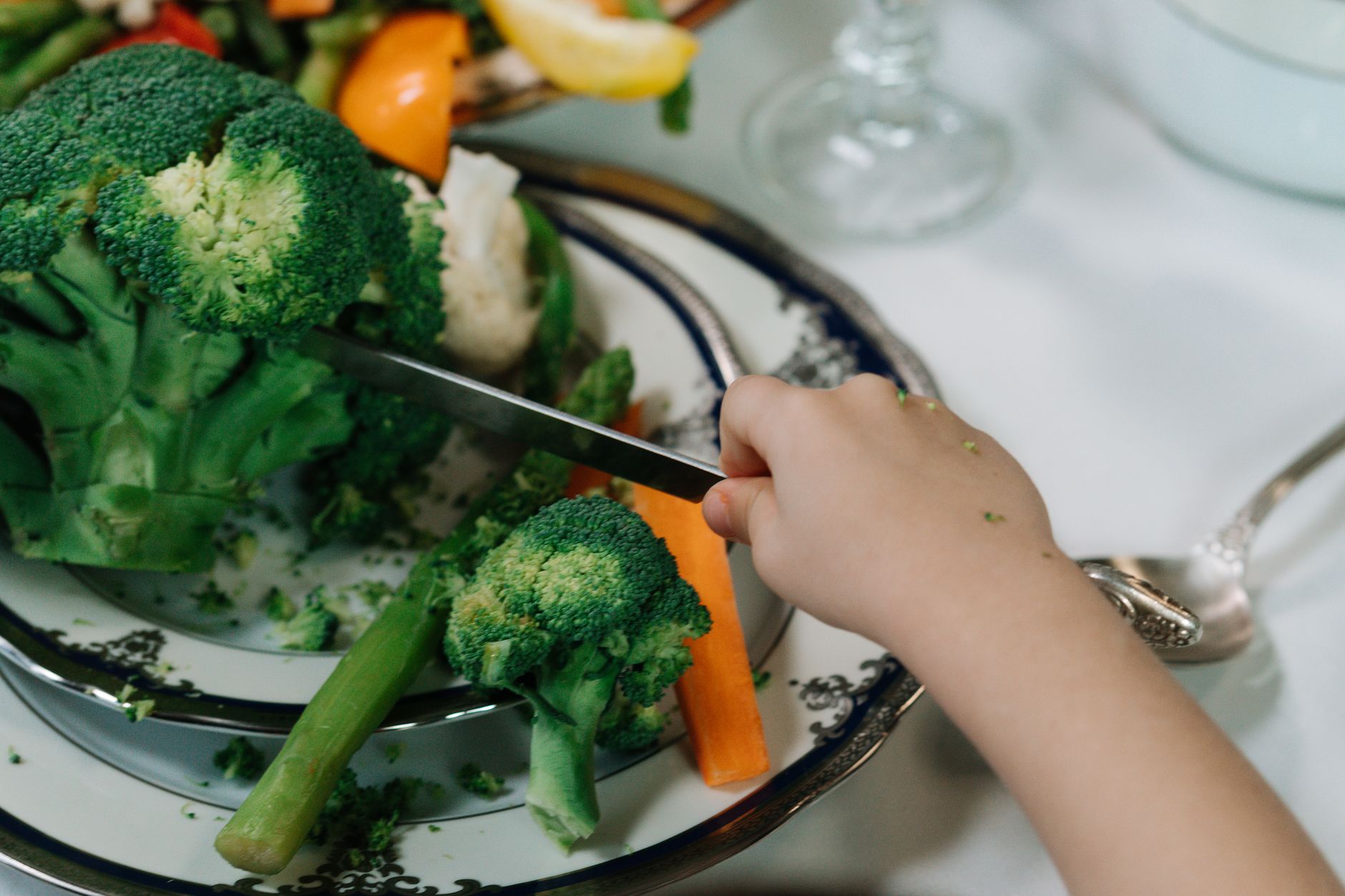 a kid cutting a broccoli with a knife